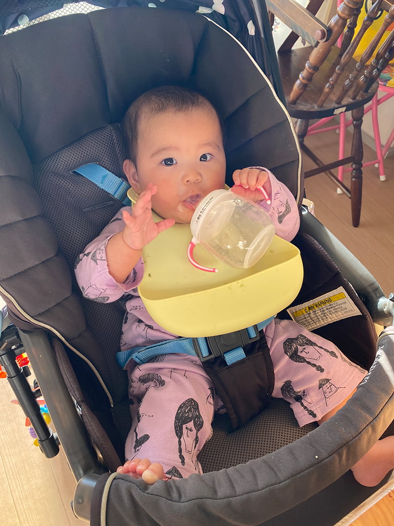 ベビーチェアに座って水をのむ赤ちゃんの写真
